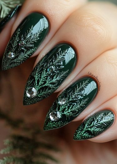 Elegant deep green stiletto nail art featuring intricate fern patterns and sparkling rhinestones.