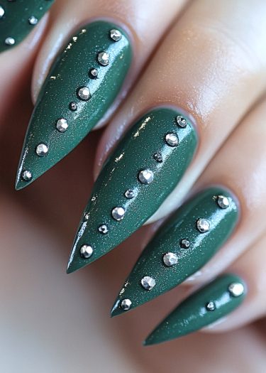 Elegant deep green almond nails adorned with shimmering metallic studs for a stunning manicure.