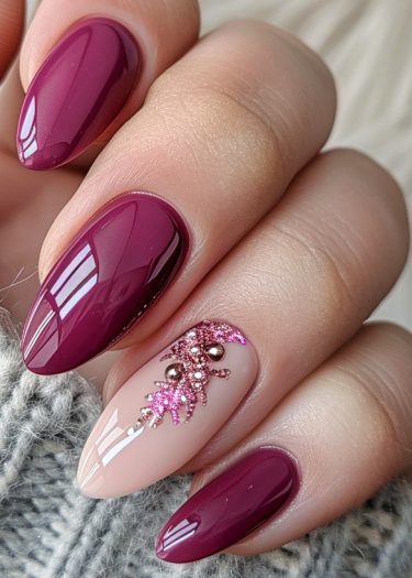 Elegant deep maroon almond nails with intricate glitter design and metallic accents.