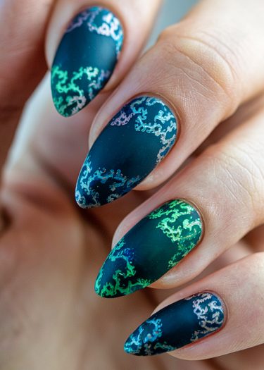 Elegant stiletto nails featuring intricate matte blue designs with vibrant iridescent patterns.