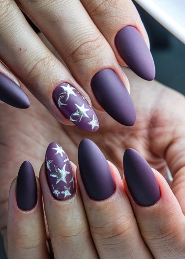 Elegant deep plum matte nails with silver star designs for a sophisticated manicure look.