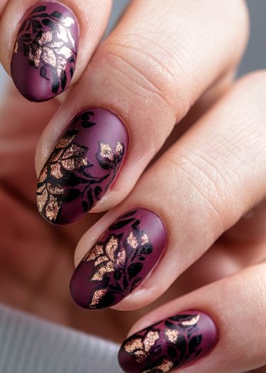 Luxurious burgundy floral nail art with black patterns and gold accents on almond-shaped nails.