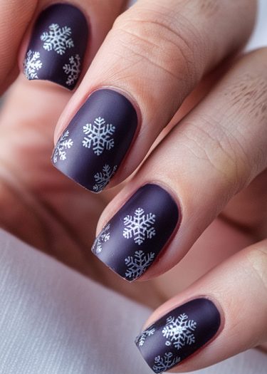 Elegant deep purple matte nails with intricate white snowflake designs for a festive winter look.