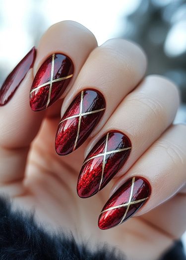 Elegant almond-shaped nails with metallic red polish and gold crisscross design.