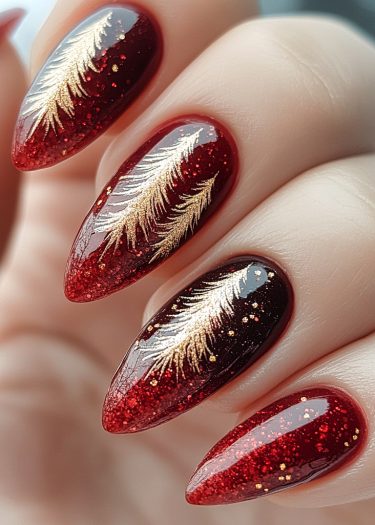 Exquisite dark red almond nails with gold feather designs and sparkling glitter accents.