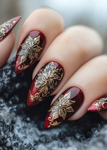 Elegant deep red stiletto nails with intricate gold floral designs for a luxurious manicure.