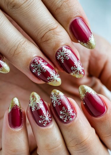 Elegant deep red almond nails with white snowflake designs and sparkling gold accents.