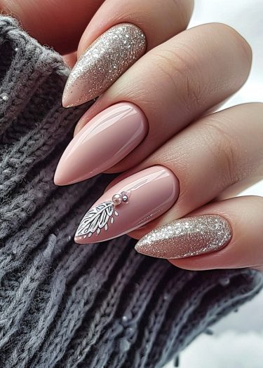 Elegant stiletto nails with nude pink, silver glitter, and intricate leaf design in cozy sweater.