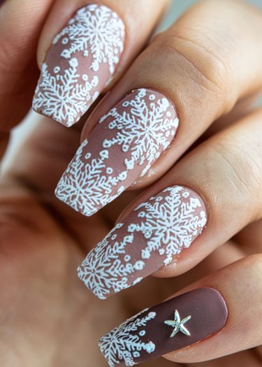 Elegant dusty pink snowflake nail art featuring intricate white designs and a star accent.