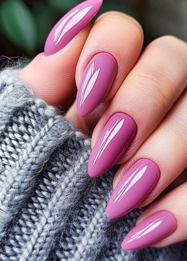 Elegant pink almond nails on manicured hands, contrasting beautifully with a cozy grey sweater.