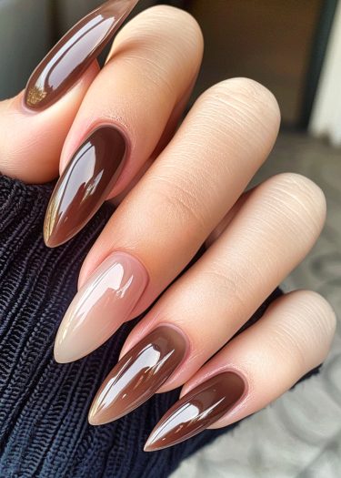 Elegant stiletto nails in earthy browns showcase a sophisticated, glossy manicure against textured fabric.