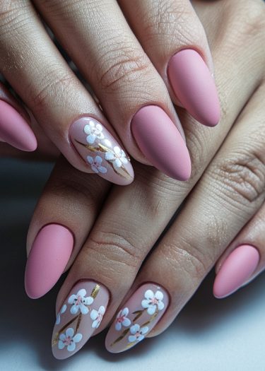 Elegant stiletto nails in matte pink with intricate floral designs and gold accents.