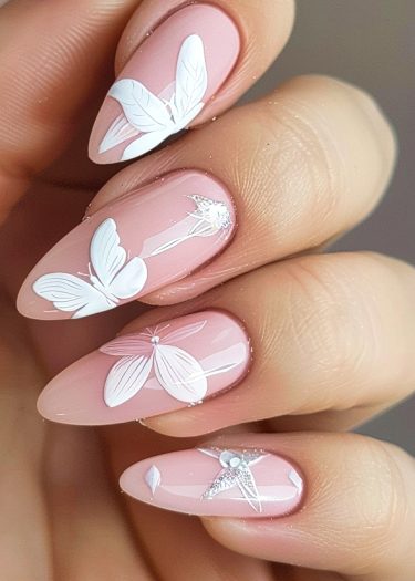 Elegant almond nail art featuring intricate white designs and sparkly accents on pastel pink polish.