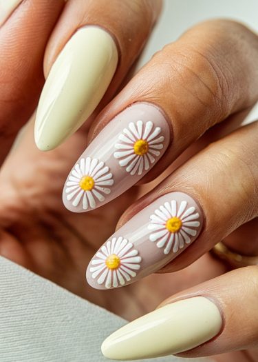 Elegant almond-shaped nails with creamy yellow polish and delicate daisy nail art.