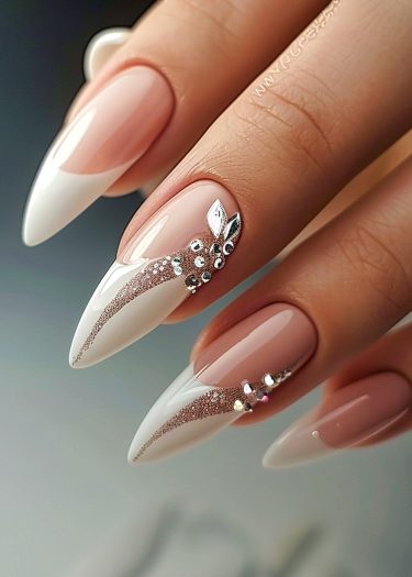 Elegant stiletto nails with French tips, rhinestones, and metallic leaf designs on a manicured hand.