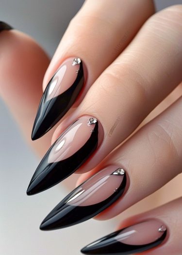 Elegant stiletto nails with nude base, black tips, and sparkling rhinestones for a glamorous look.