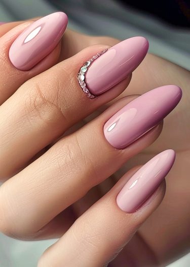 Elegant almond-shaped nails with glossy pink polish and sparkling rhinestones for a sophisticated manicure.