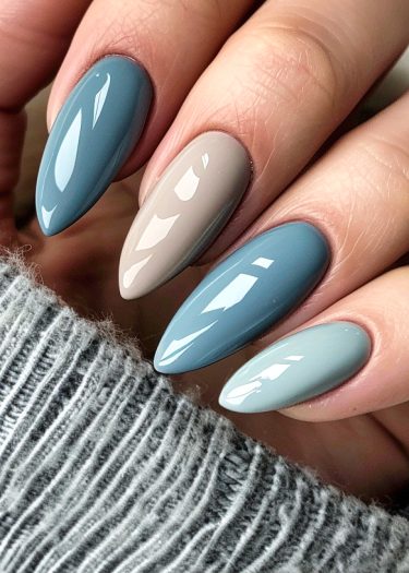 Elegant almond-shaped nails in glossy muted tones against a cozy gray fabric backdrop.