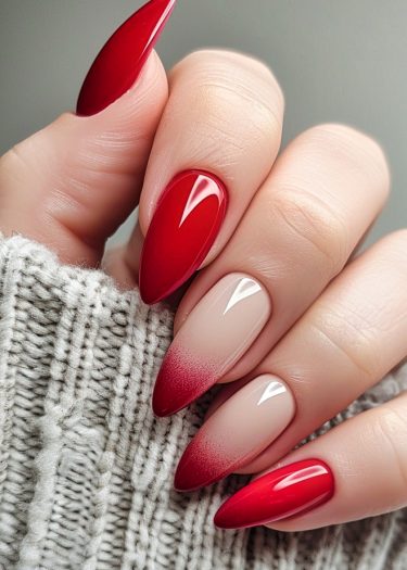 Elegant almond-shaped red nails with glossy and ombre designs against a cozy knit backdrop.