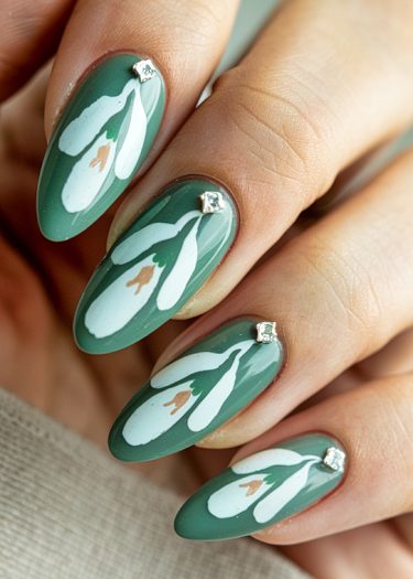 Elegant almond nails with green polish and delicate snowdrop floral designs and silver accents.