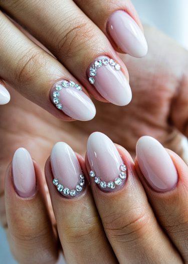 Elegant almond nails with nude-pink polish and sparkling rhinestones create a sophisticated look.