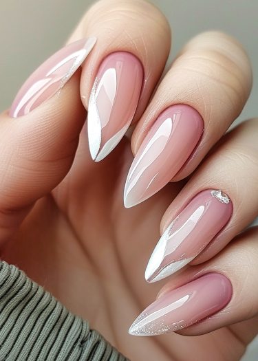 Elegant almond-shaped nails with glossy nude pink and curved white French tips adorned with rhinestones.