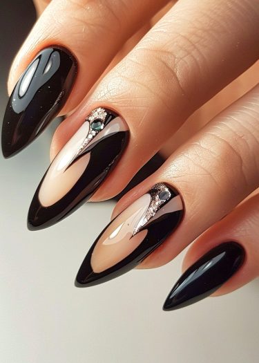 Elegant stiletto nails with glossy black and nude design, featuring rhinestones and intricate patterns.