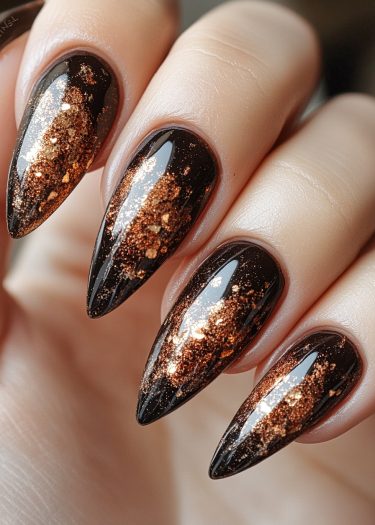 Elegant stiletto black nails with ombré gold glitter design for a glamorous look.