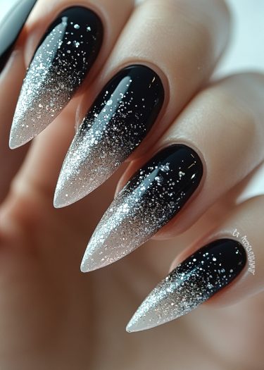 Stiletto black nails with shimmering silver glitter gradient for a glamorous manicure.