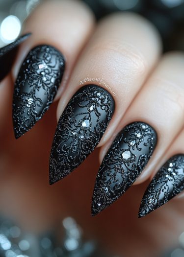 Elegant black lace nails with stiletto shape, featuring intricate designs and sparkling rhinestones.