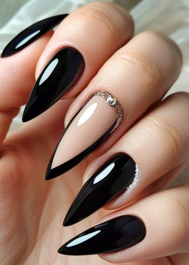 Elegant black stiletto nails with glitter and rhinestone embellishment for a chic manicure look.