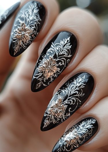 Elegant black nail art features intricate silver and gold floral designs on pointed stiletto nails.