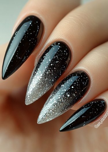 Elegant black stiletto nails featuring a shimmering silver glitter gradient for a bold manicure.