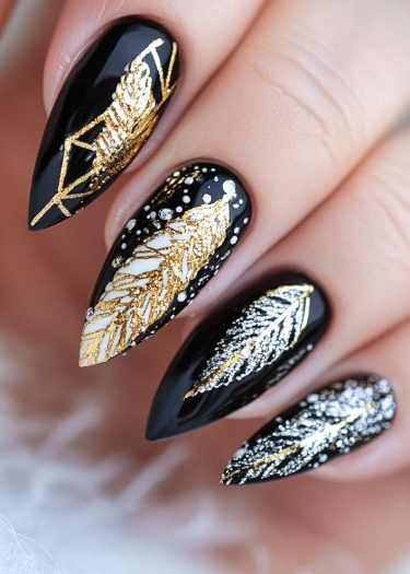 Elegant black stiletto nails with intricate gold and white nature-inspired designs for a luxurious look.