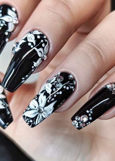 Elegant black and white nail art with floral designs and sparkling rhinestones for a chic look.