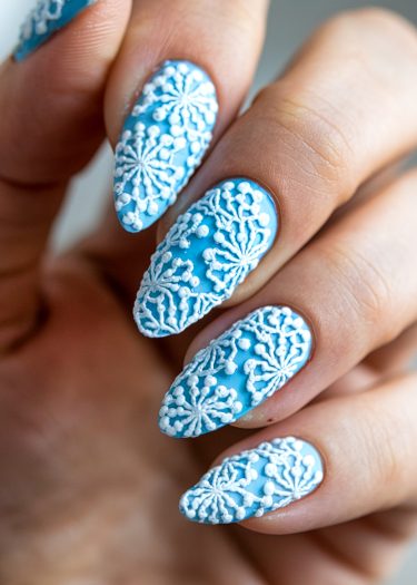 Elegant blue stiletto nails featuring intricate white lace patterns and a glossy finish.