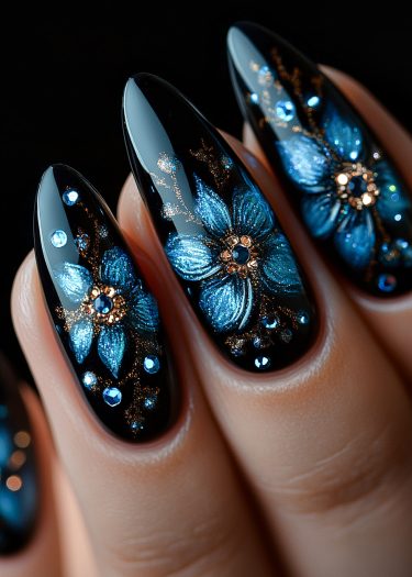 Elegant blue flower nail art on glossy black almond-shaped nails with golden accents and rhinestones.