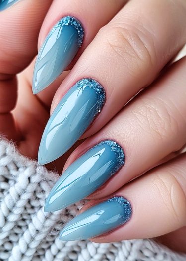 Elegant blue glitter nails with almond shape and glossy finish on a cozy background.