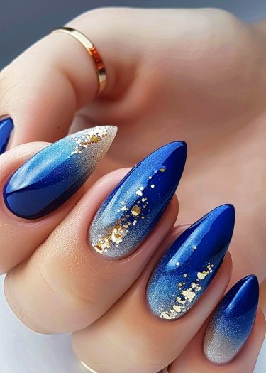 Glamorous blue gradient nails with gold embellishments and rings on elegant fingers.