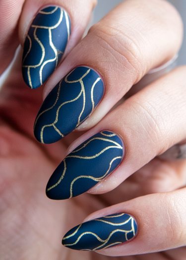 Elegant navy blue almond-shaped nails with intricate gold designs for a sophisticated look.