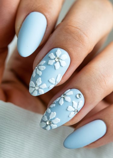 Elegant blue nail art with 3D floral designs and rhinestones on well-manicured hands.