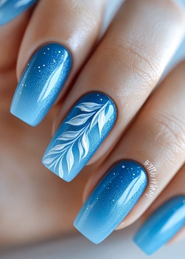 Elegant blue ombre nails with intricate leaf design and sparkling details create a stunning manicure.