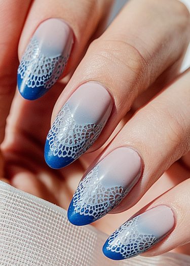 Elegant blue French tip nail art with intricate lace design on almond-shaped nails.