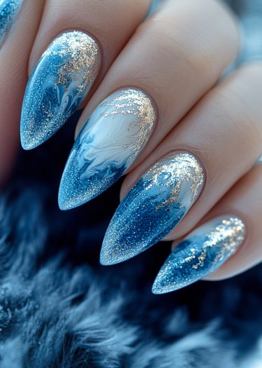 Stiletto nails featuring a luxurious blue and silver marble design with gold leaf accents.