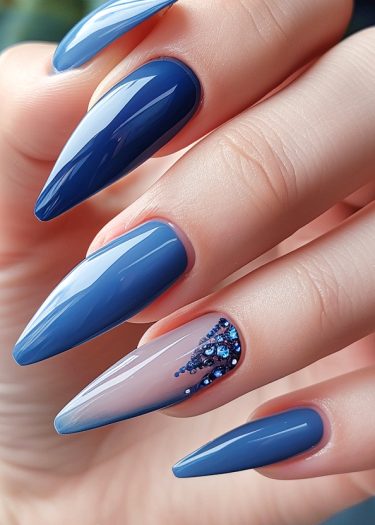 Stunning stiletto nails in glossy blue with a sparkling accent design on a manicured hand.