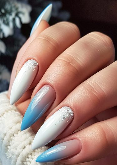 Elegant stiletto nails feature blue gradient and white embellishments for a chic manicure look.