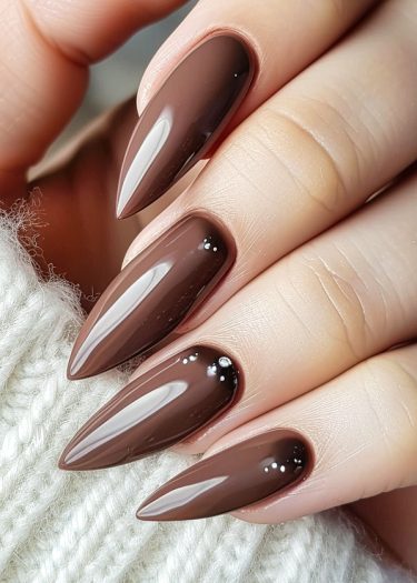 Elegant stiletto nails in glossy chocolate brown resting on cozy knit fabric.