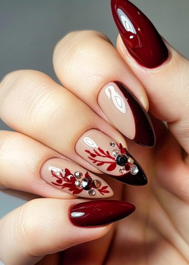 Elegant burgundy almond nails with detailed art and rhinestones for a sophisticated manicure look.