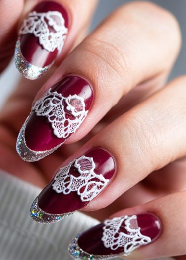 Elegant burgundy nail art with lace patterns and glitter tips showcases sophisticated nail design.