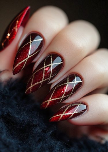 Elegant almond-shaped burgundy nails feature gold crisscross patterns for a luxurious look.